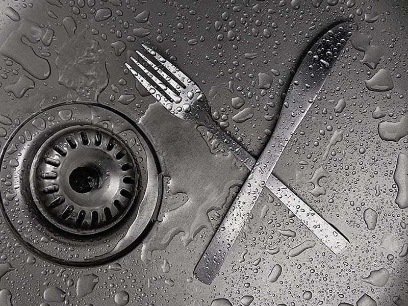 A fork and knife sitting in a stainless steel sink basin. 