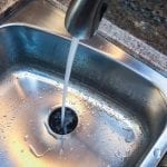 A sink faucet runs into a stainless steel basin with a garbage disposal.