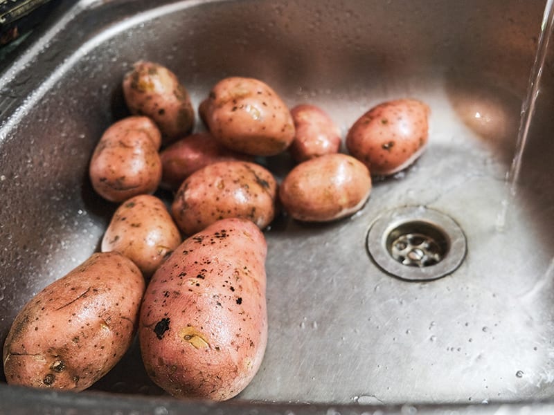Potatoes are being washed in a stainless steel sink basin. 