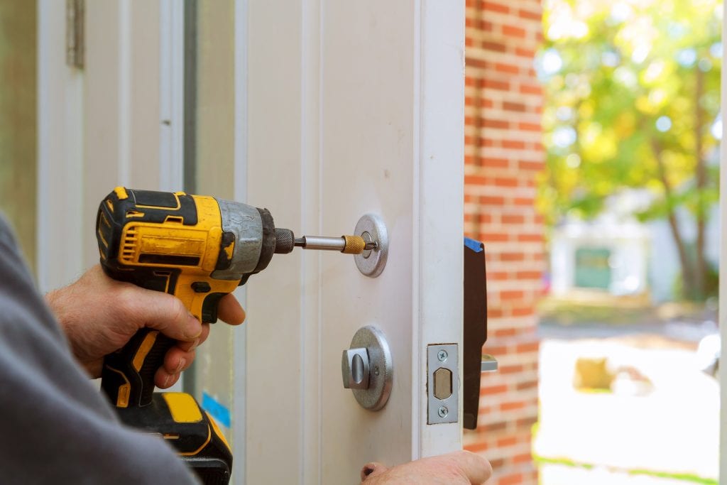 worker's hands installing new door locker man repairing the doorknob. closeup drill